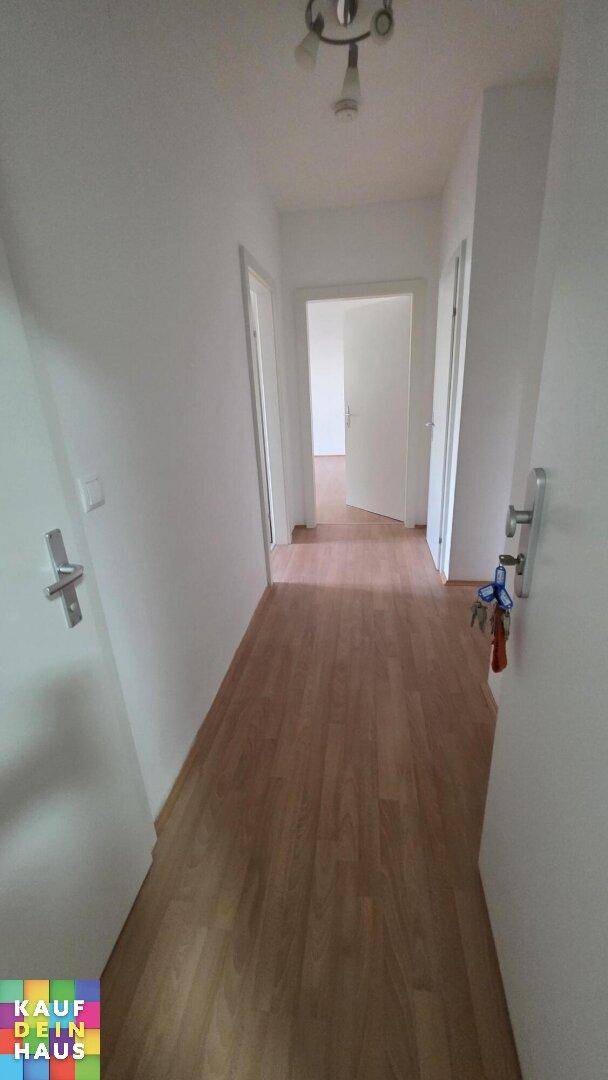 Heller Flur mit Laminatboden und weißen Wänden, der zu verschiedenen Räumen führt.