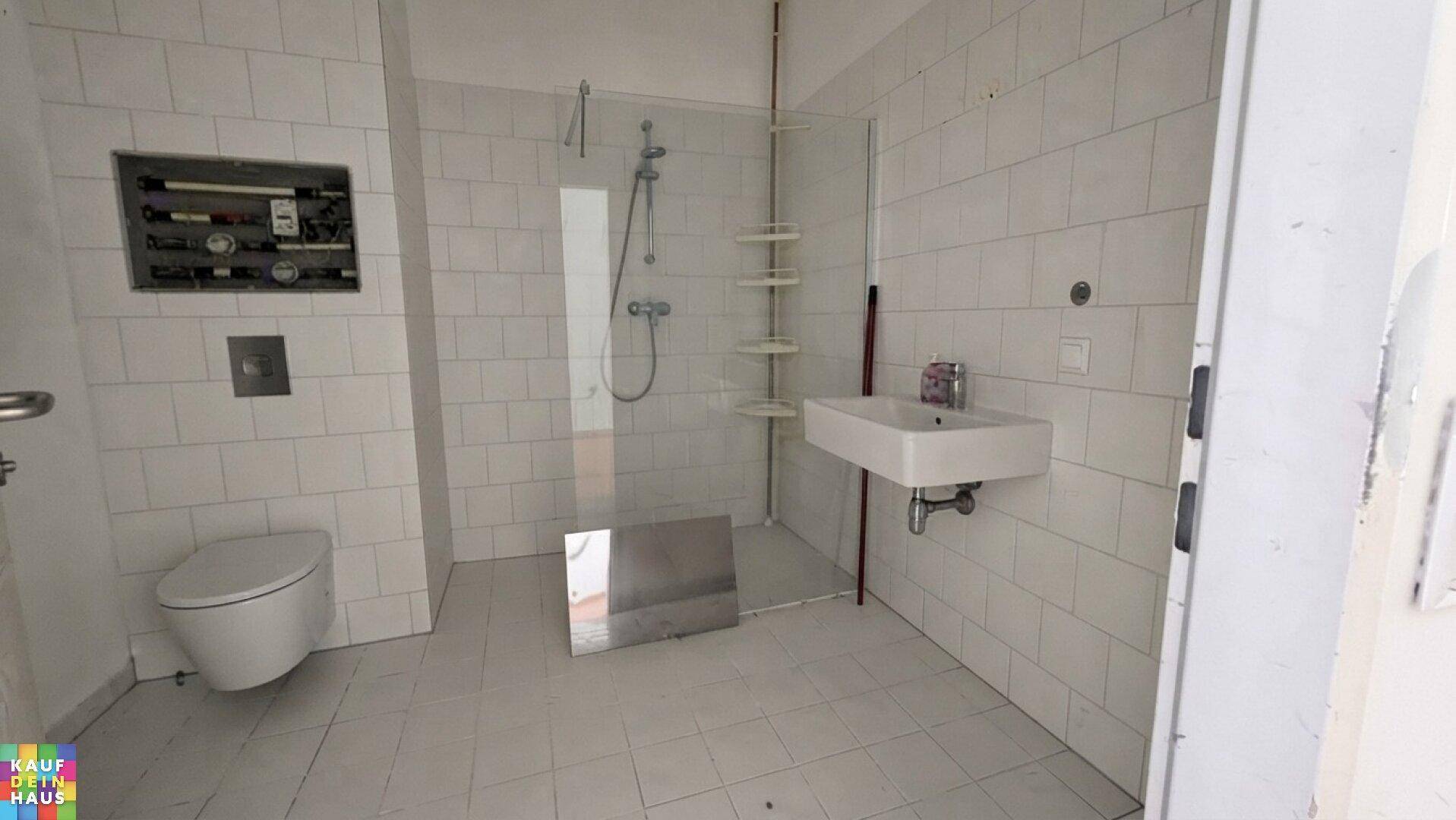 Modernes Badezimmer mit weißen Fliesen, ebenerdiger Dusche, WC und Waschtisch.
