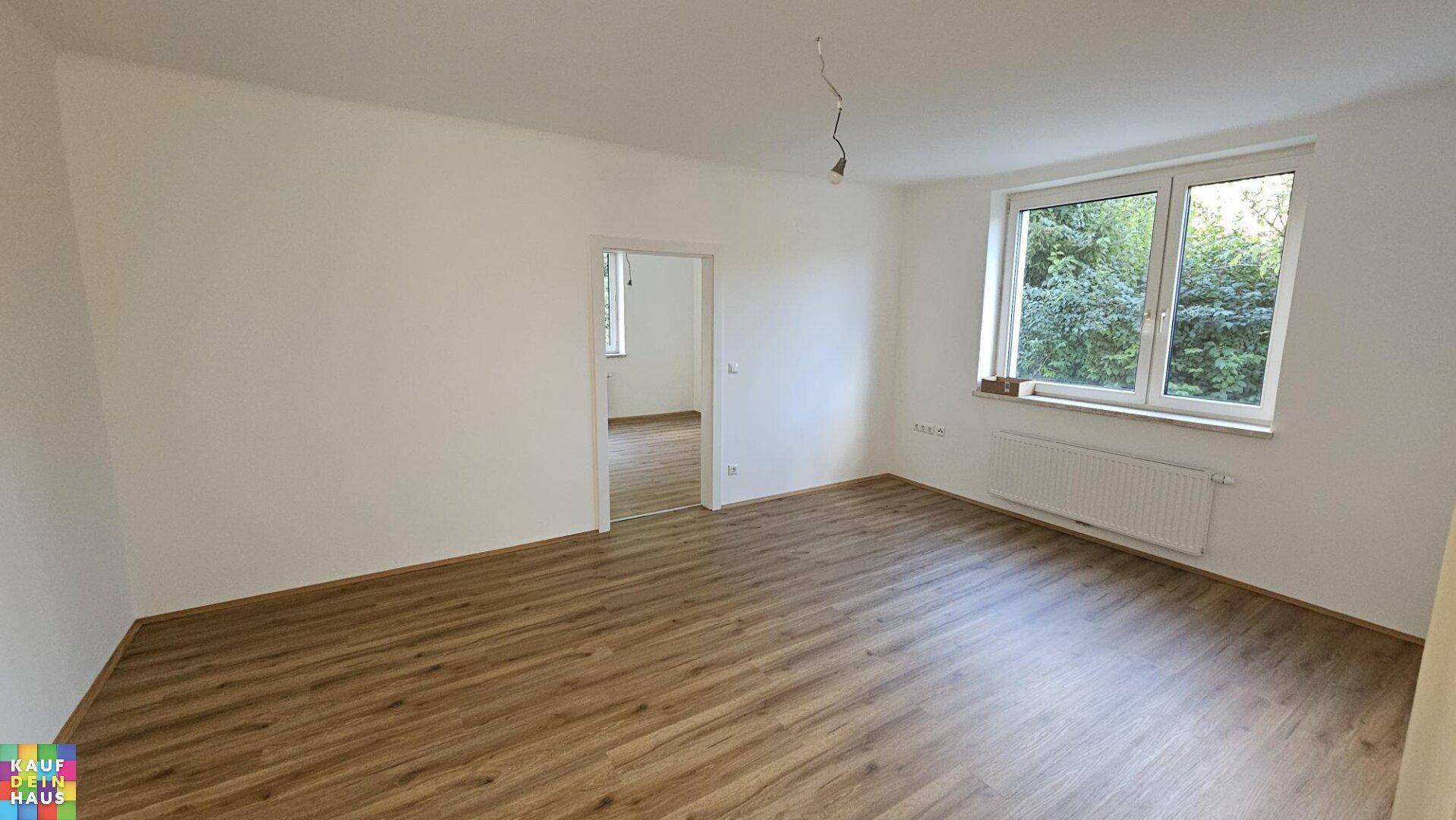 Heller Wohnraum mit Laminatboden, weißen Wänden und Blick ins Grüne.