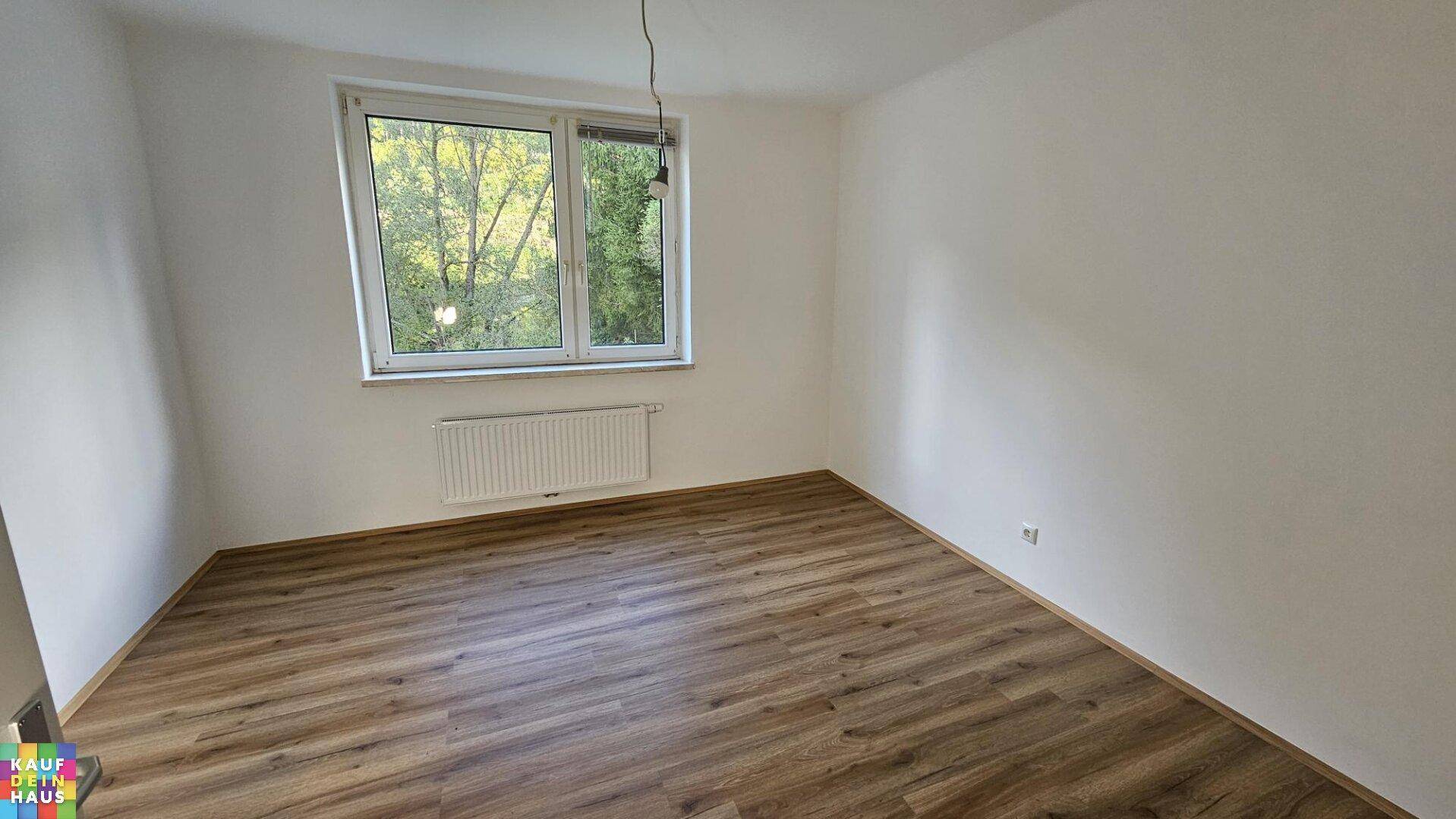 Schlafzimmer mit Laminatboden, weiß gestrichenen Wänden und Fenster mit Blick ins Grüne.