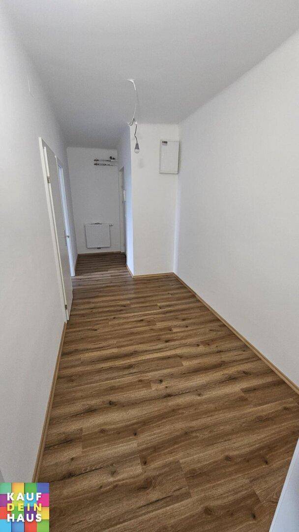Heller Flur mit Laminatboden und weißen Wänden, der zu verschiedenen Räumen führt.