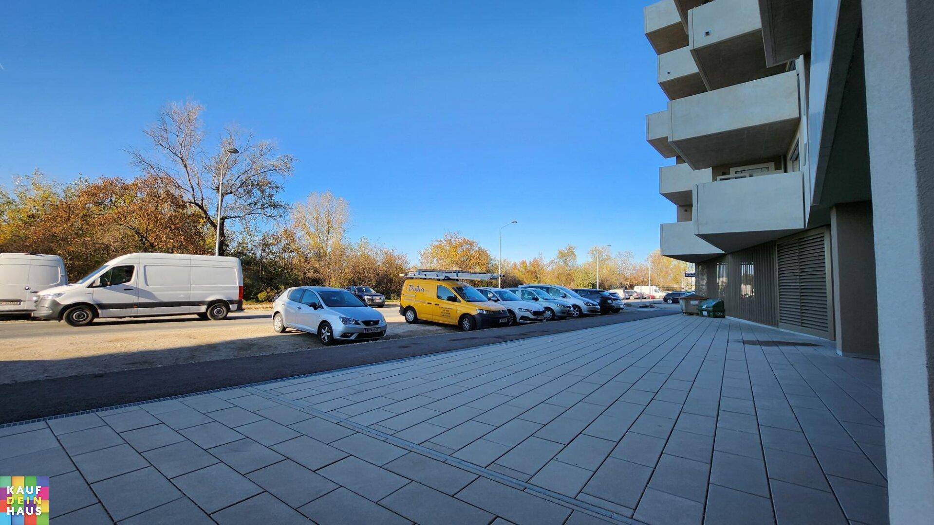 Gepflasterter Außenbereich mit parkenden Autos und der Seitenansicht eines modernen Gebäudes.