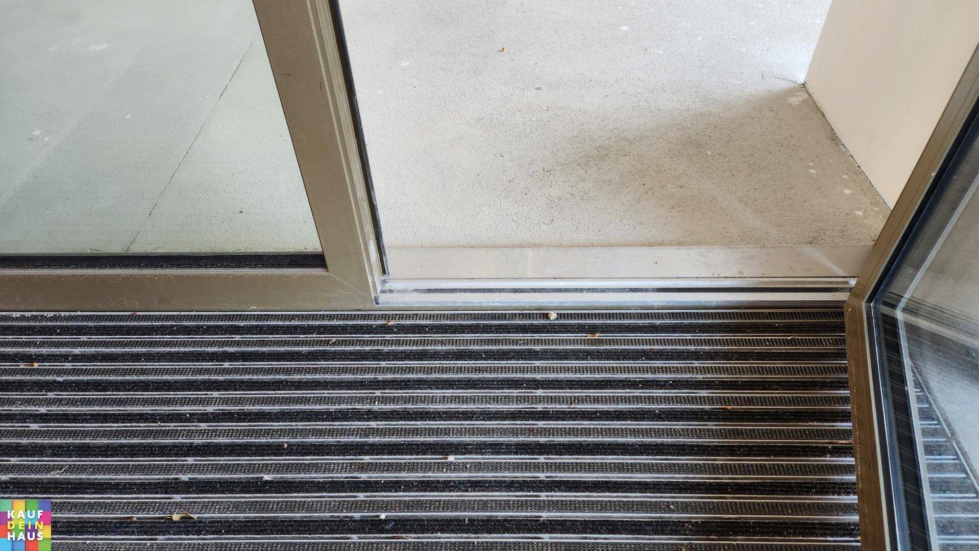 Nahaufnahme einer Fußmatte am Eingangsbereich mit einer modernen Glastür.
