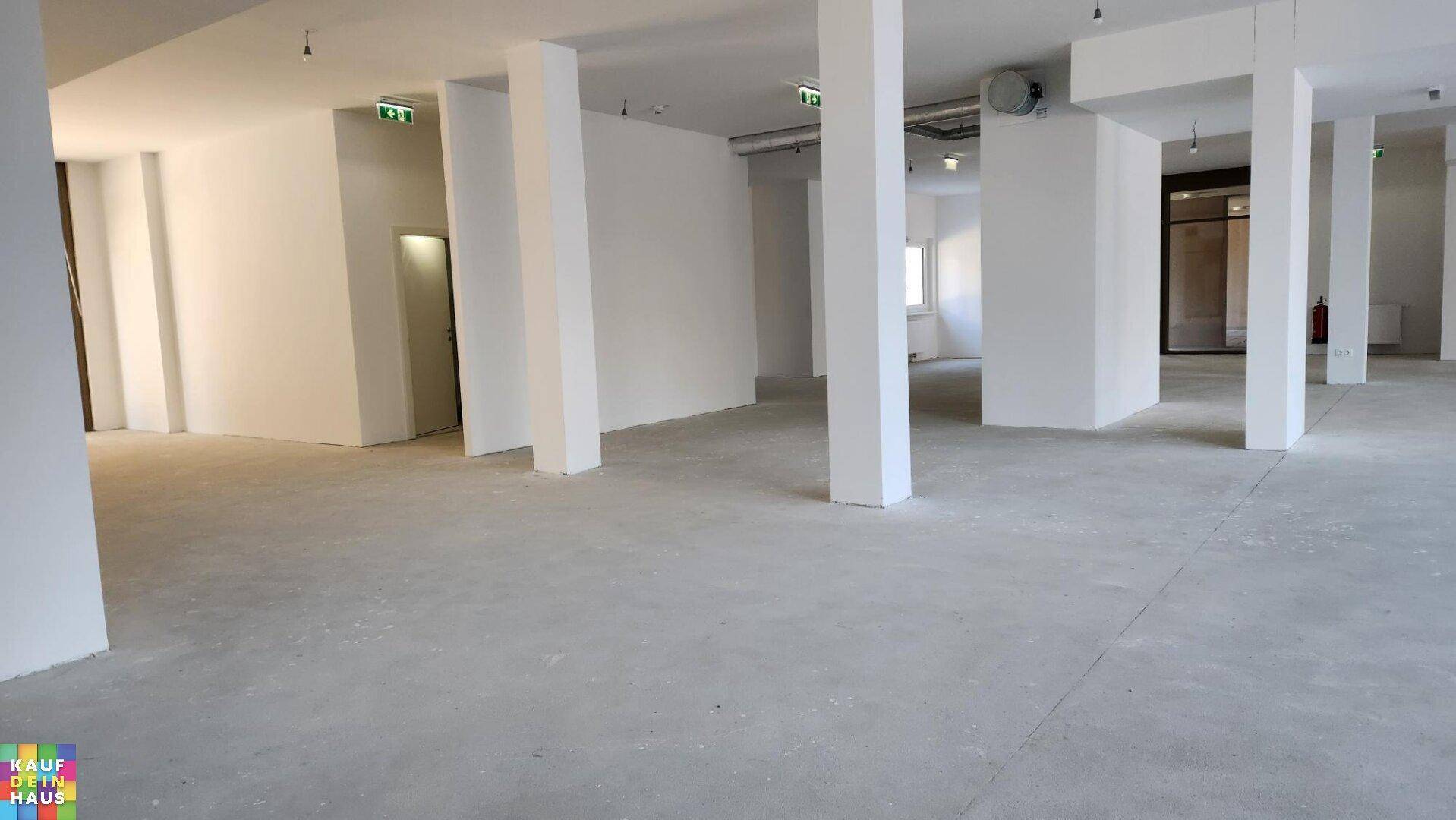 Großer, leerer Gewerberaum mit Betonboden, weißen Wänden und tragenden Säulen.
