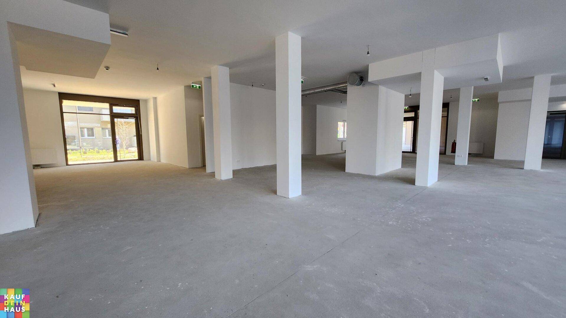 Heller Gewerberaum mit Betonboden, weißen Wänden und großen Glastüren zum Außenbereich.