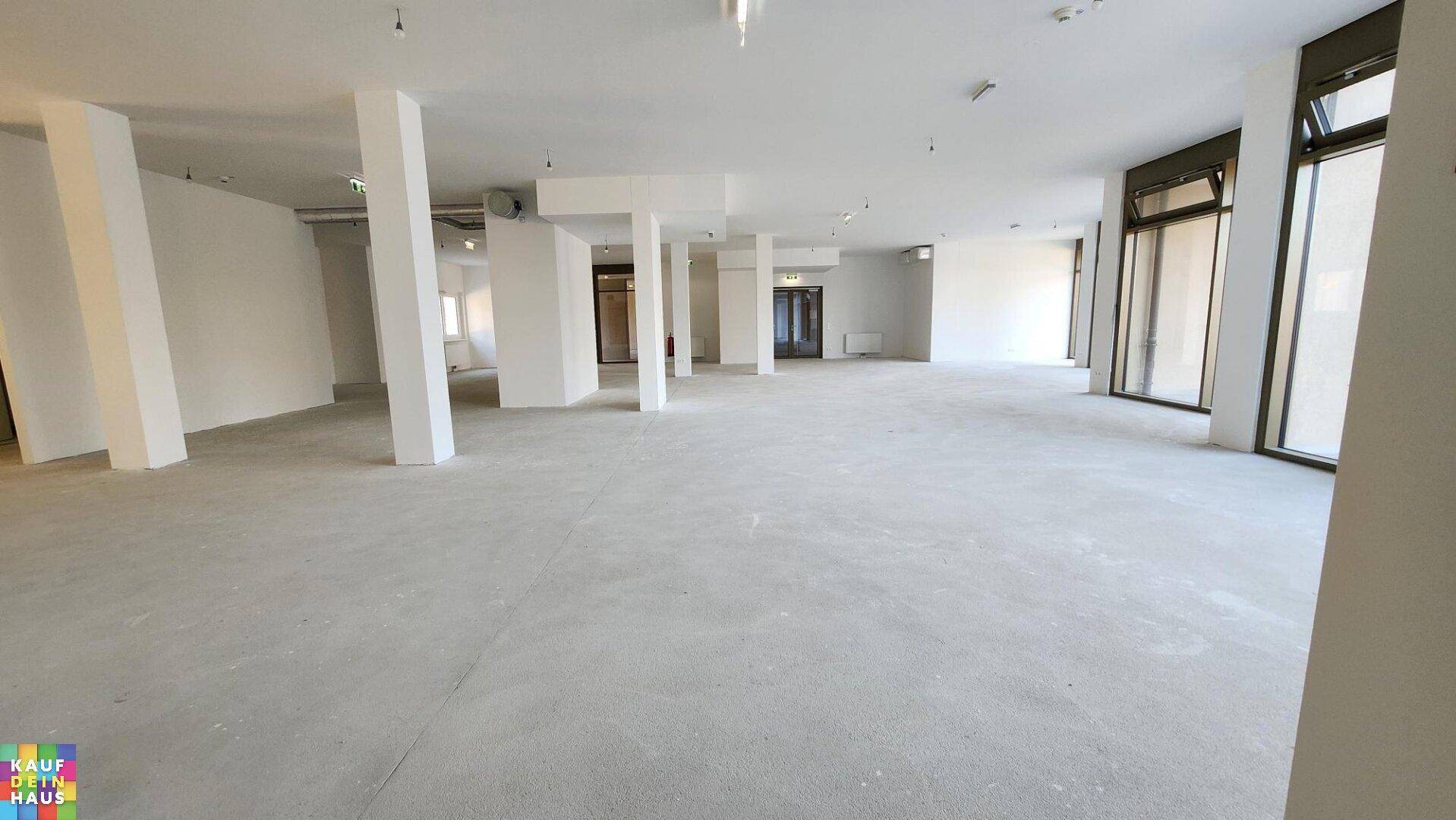 Geräumiger Gewerberaum mit großen Fensterfronten, Betonboden und weißen Wänden.