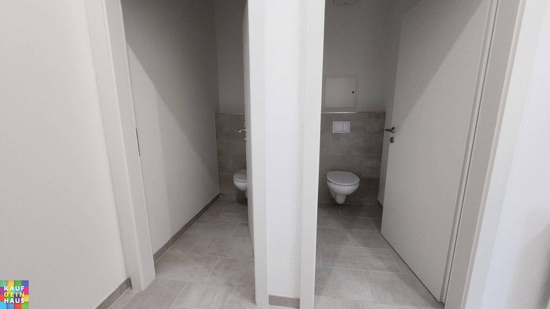 Zwei separate Toilettenräume mit modernen Wand-WCs und gefliesten Wänden.