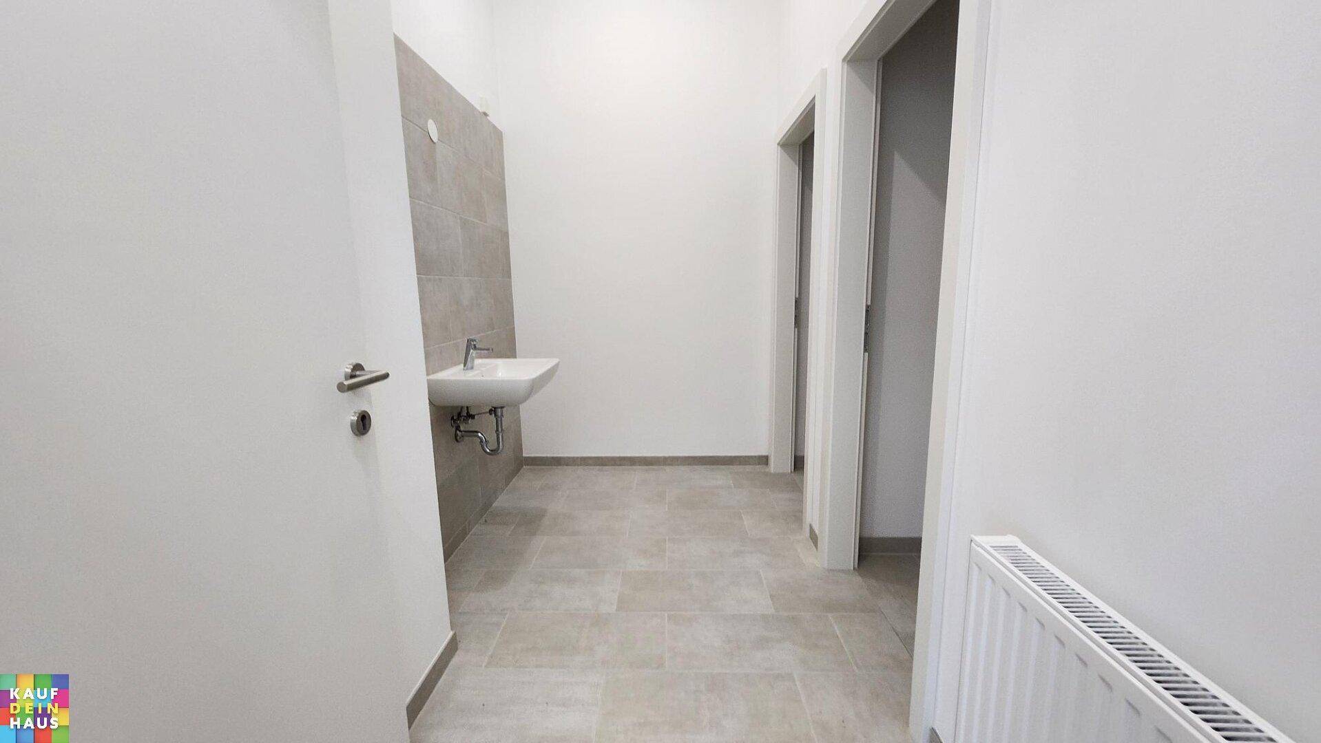 Toilettenraum mit Waschbecken, Heizkörper und hellen Fliesen an Boden und Wand.
