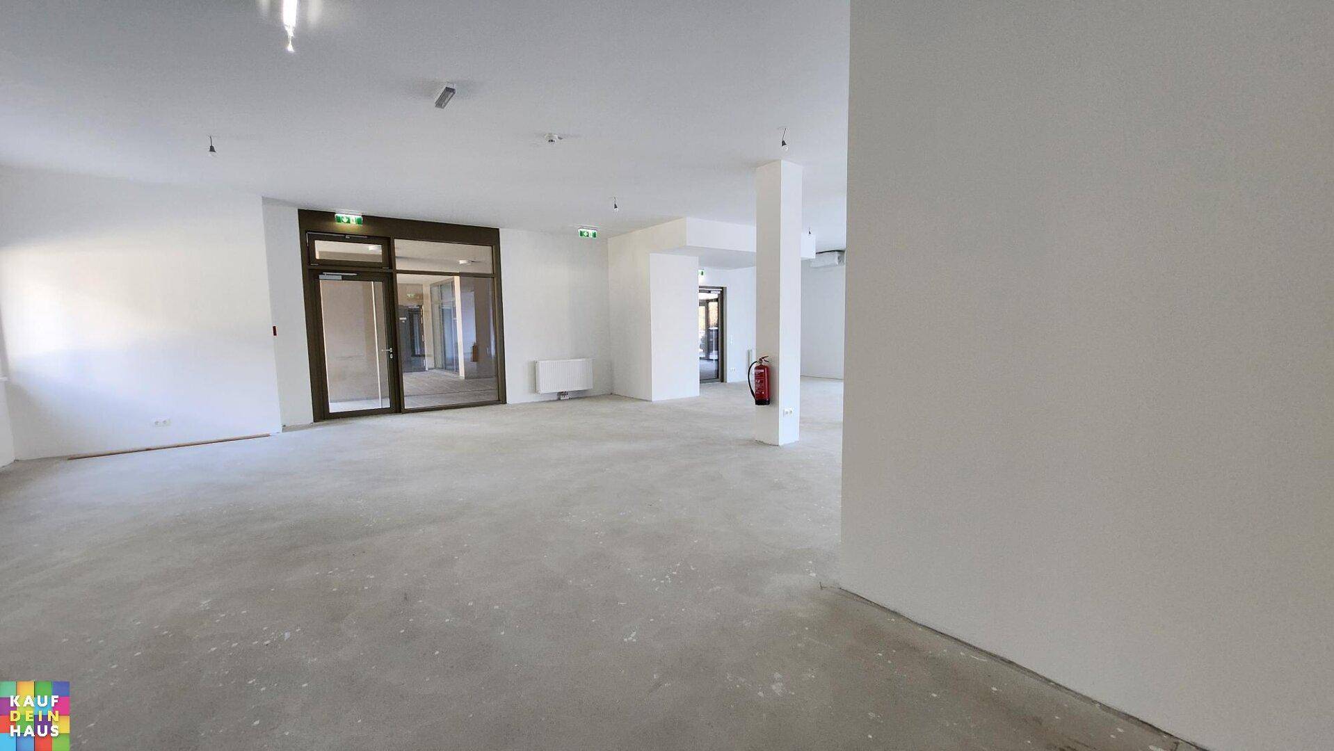 Geräumiger Gewerberaum mit Betonboden, weißen Wänden und einem Feuerlöscher im Vordergrund.