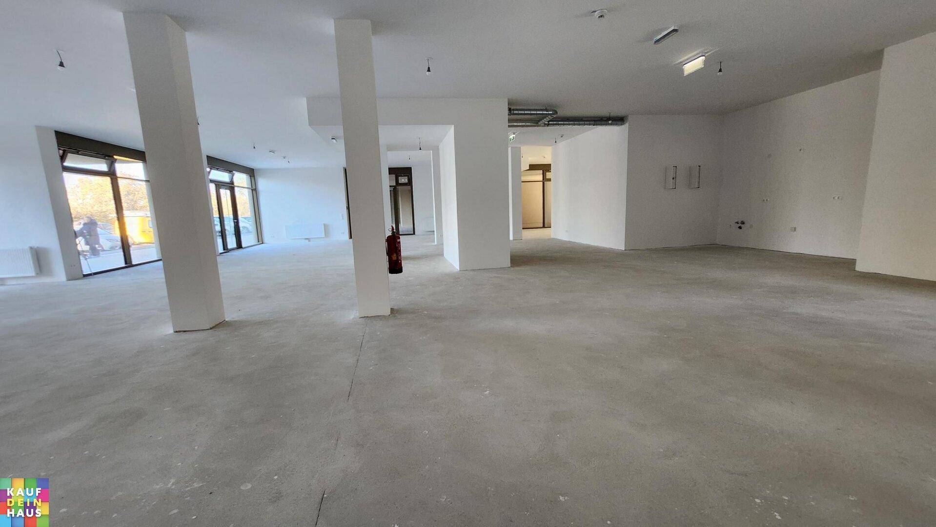 Großer Gewerberaum mit Betonboden, weißen Wänden und sichtbaren Leitungen an der Decke.