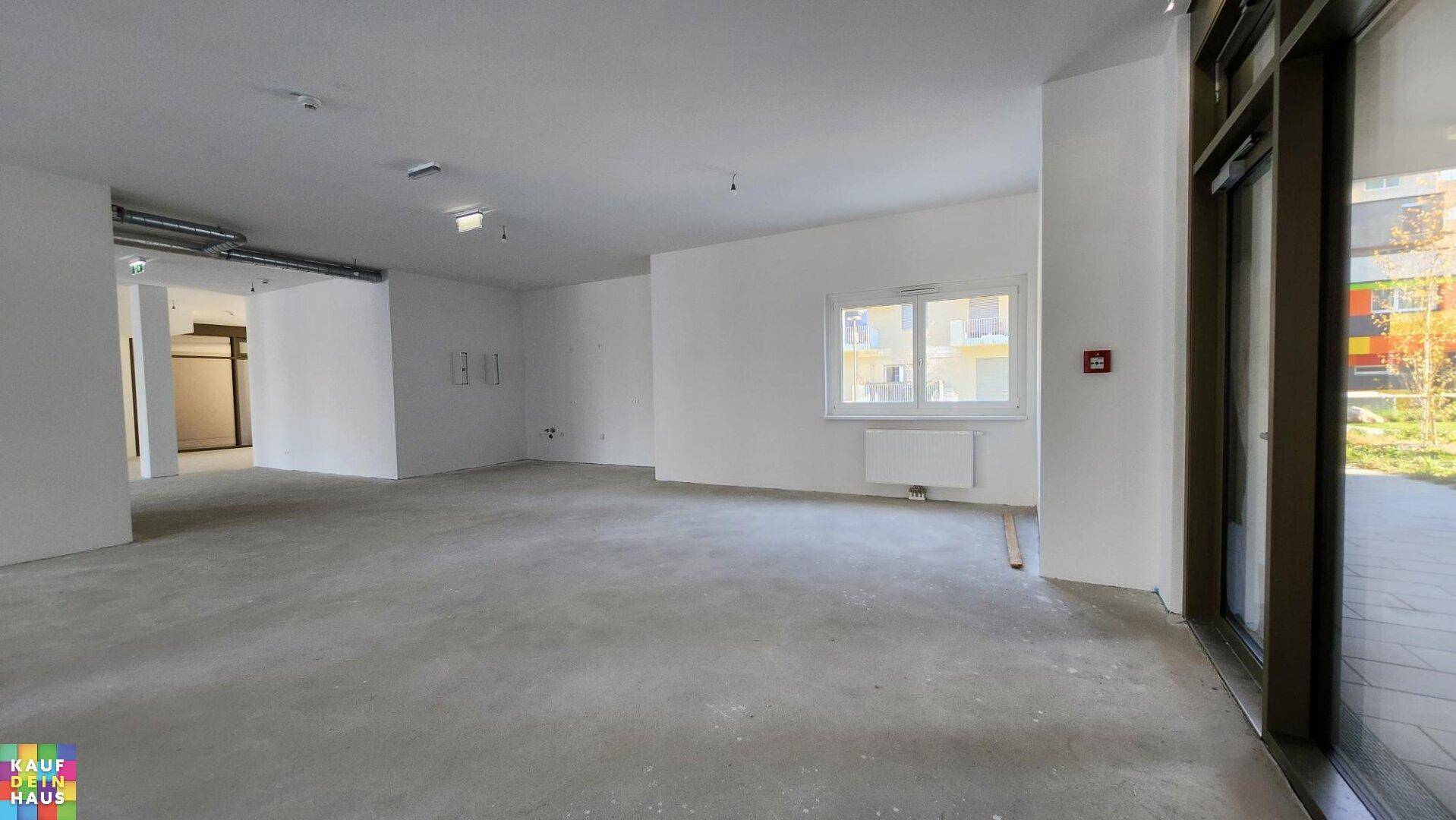 Heller Gewerberaum mit Betonboden, weißen Wänden, einem Fenster und einem Heizkörper.