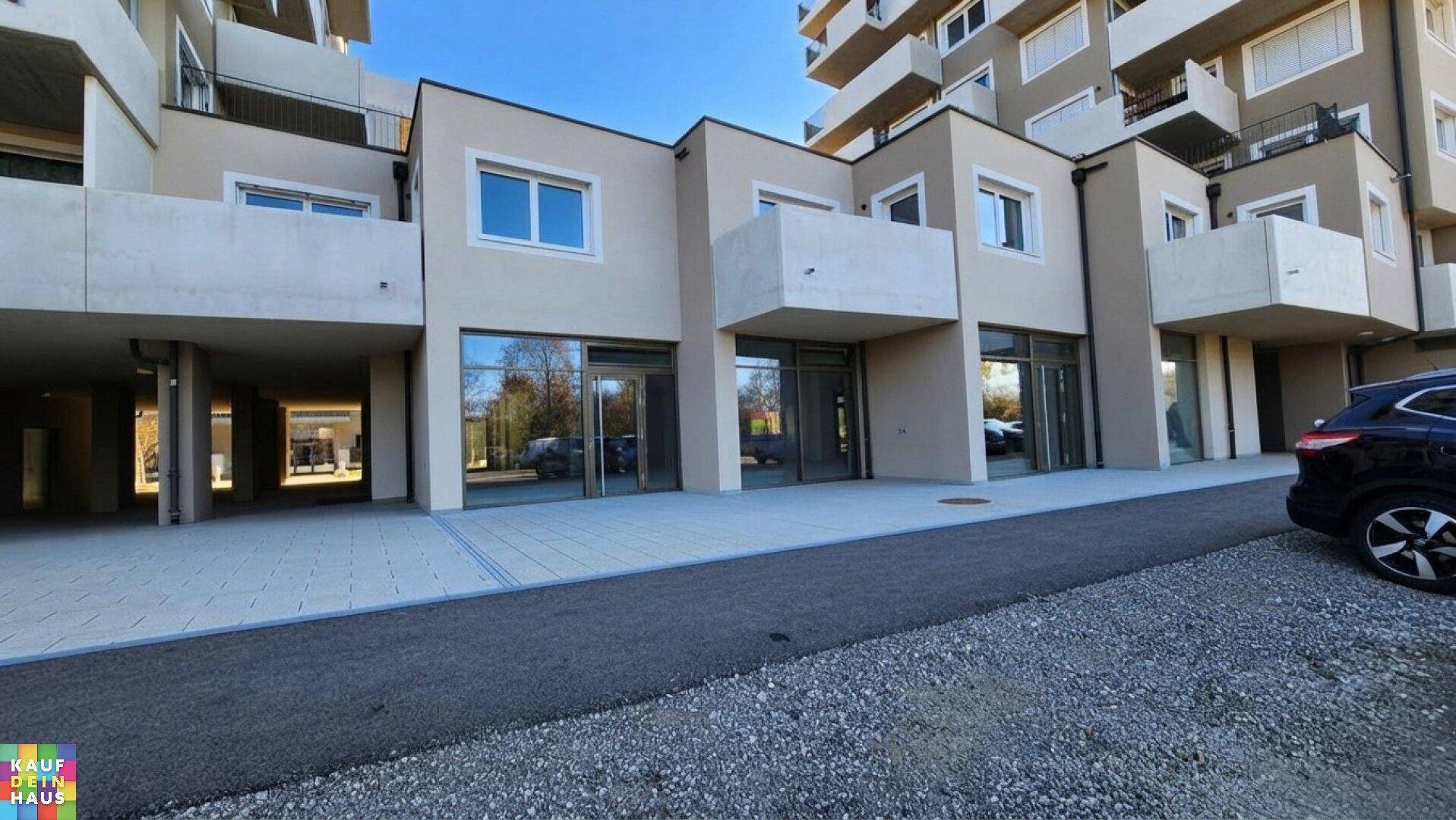 Fassade des modernen Gebäudes mit großen Schaufenstern im Erdgeschoss und kleinen Balkonen darüber.