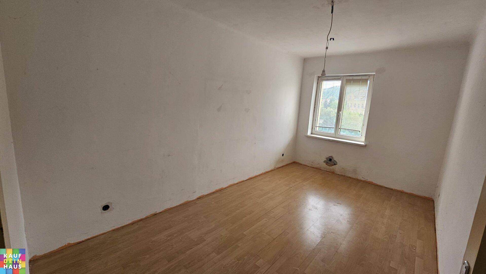 Leerer Raum mit weißen Wänden, einem Fenster und Laminatboden, bereit für die weitere Renovierung.