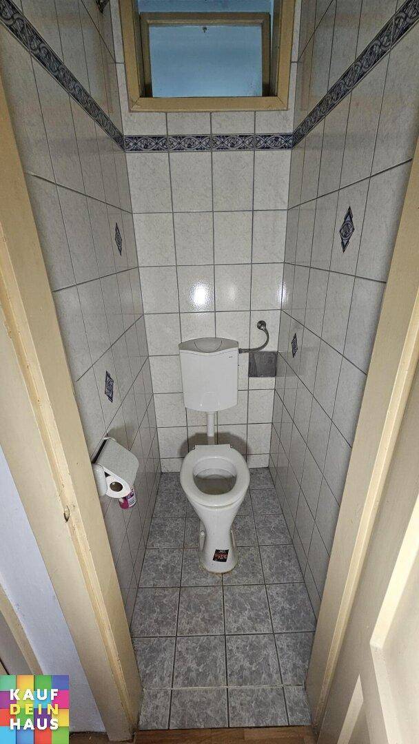Kleines WC mit grauen Fliesen, Toilette und einem kleinen Fenster für natürliche Belüftung.