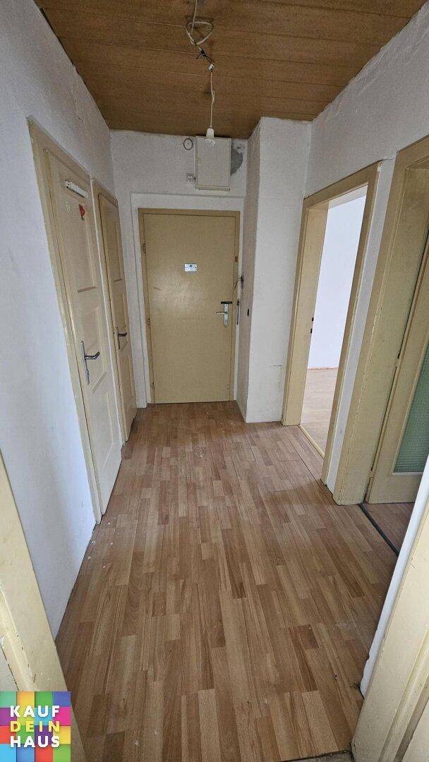 Flur mit Laminatboden und Holzdeckenverkleidung, der zu mehreren Zimmern führt.