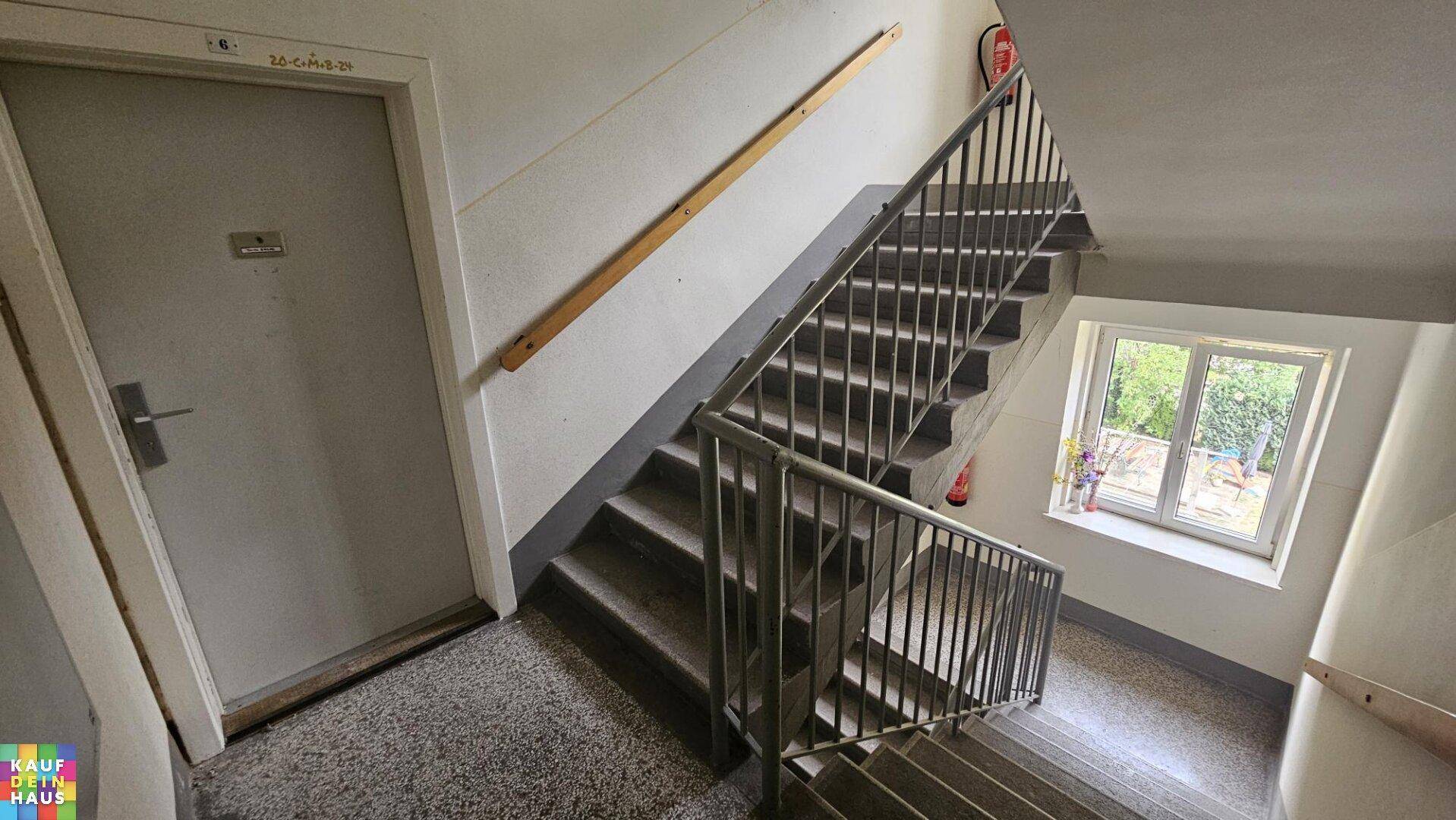 Treppenhaus mit Metallgeländer und Fenster, das natürliches Licht in den Gemeinschaftsbereich bringt.