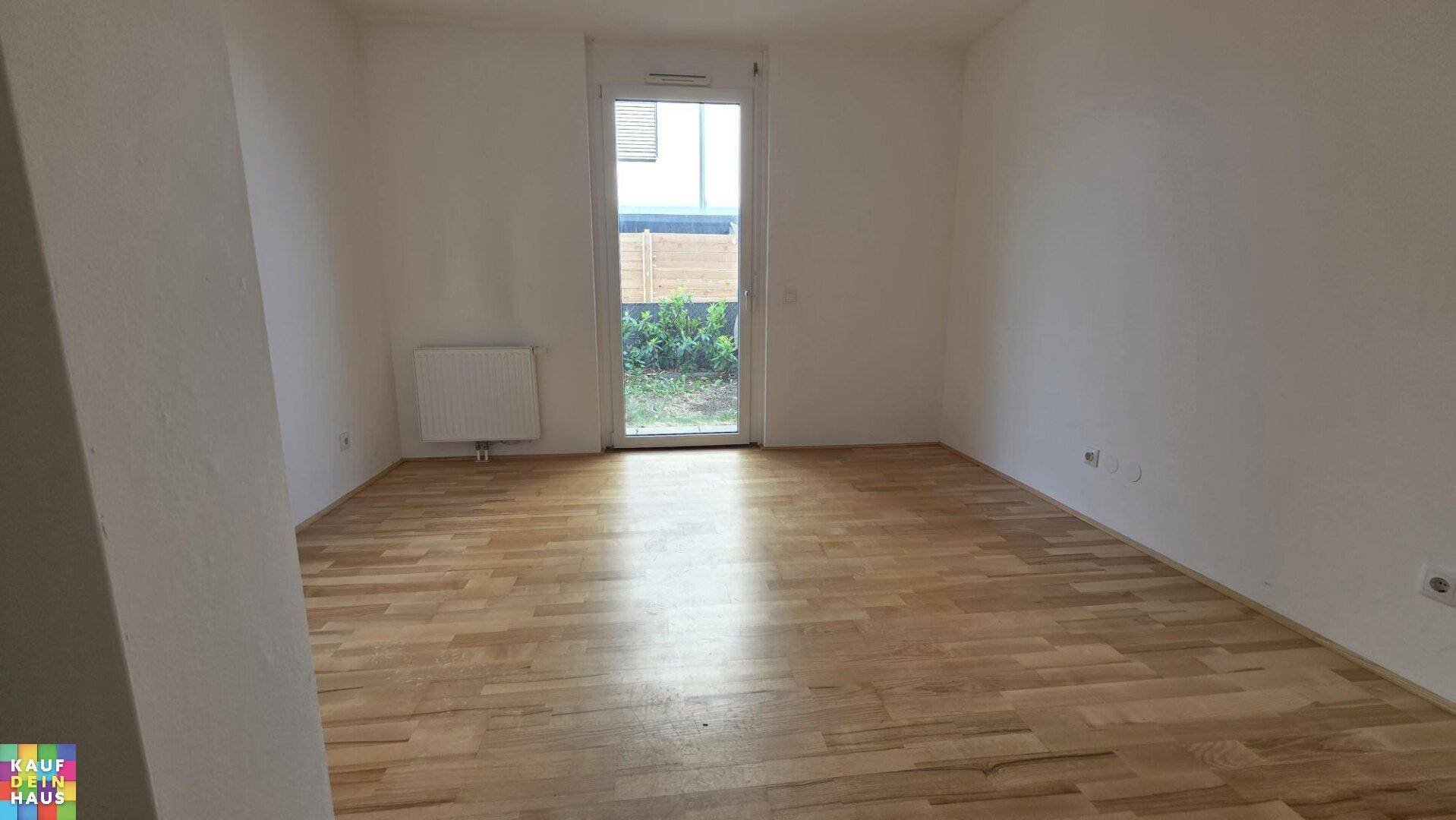 Helles, leeres Zimmer mit Parkettboden und Zugang zu einem kleinen Außenbereich.