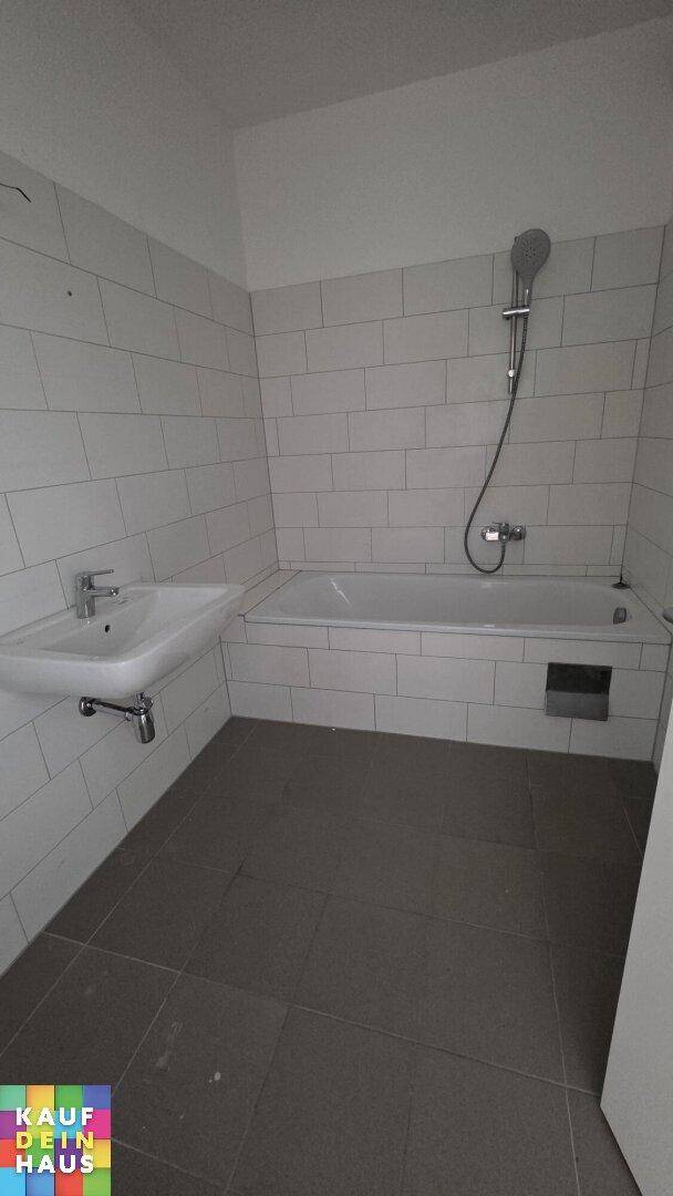 Modern gefliestes Badezimmer mit Badewanne und Waschbecken in hellen Farbtönen.