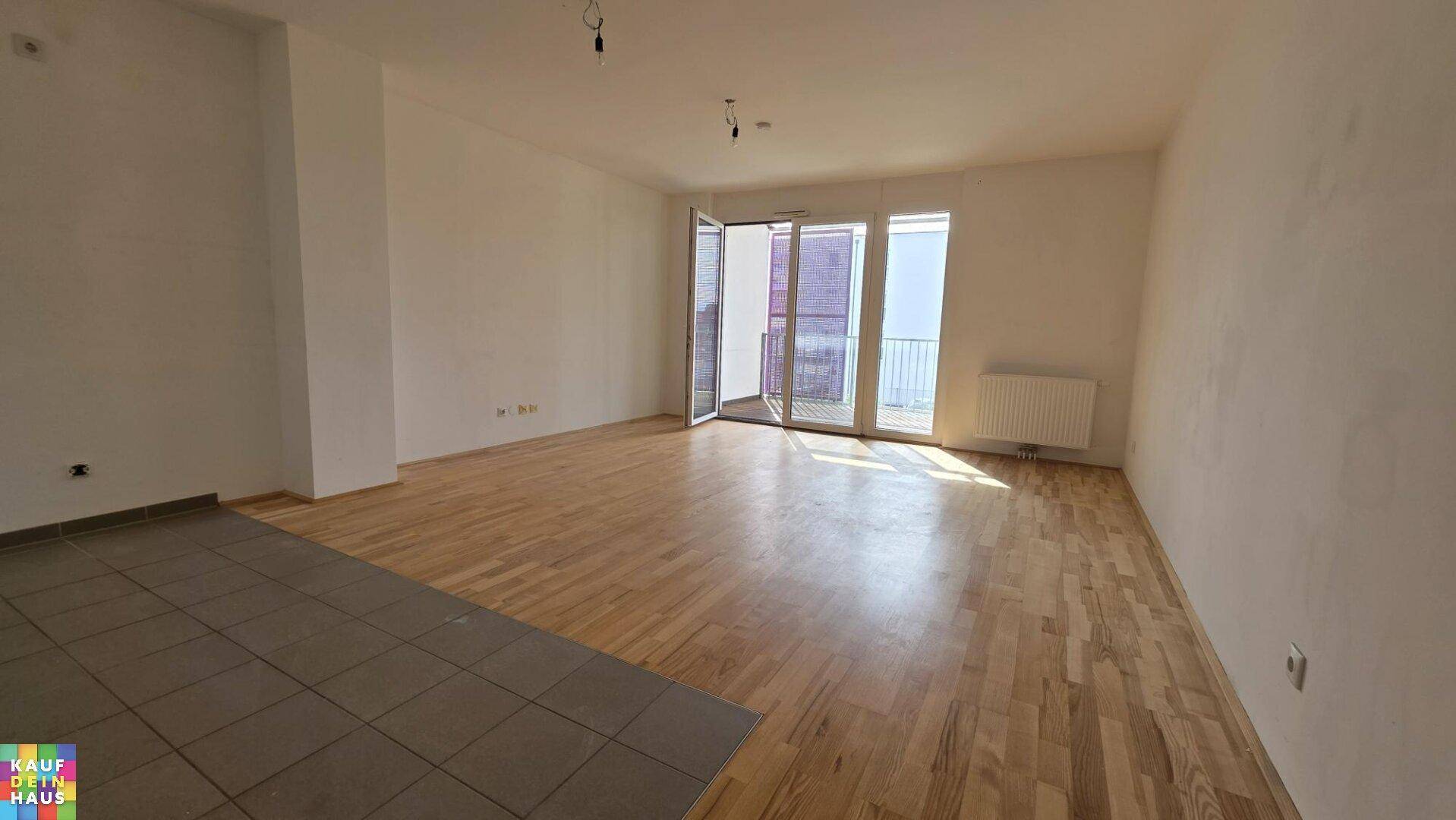 Geräumiges Wohnzimmer mit Parkett- und Fliesenboden, bietet Zugang zu einem Balkon.