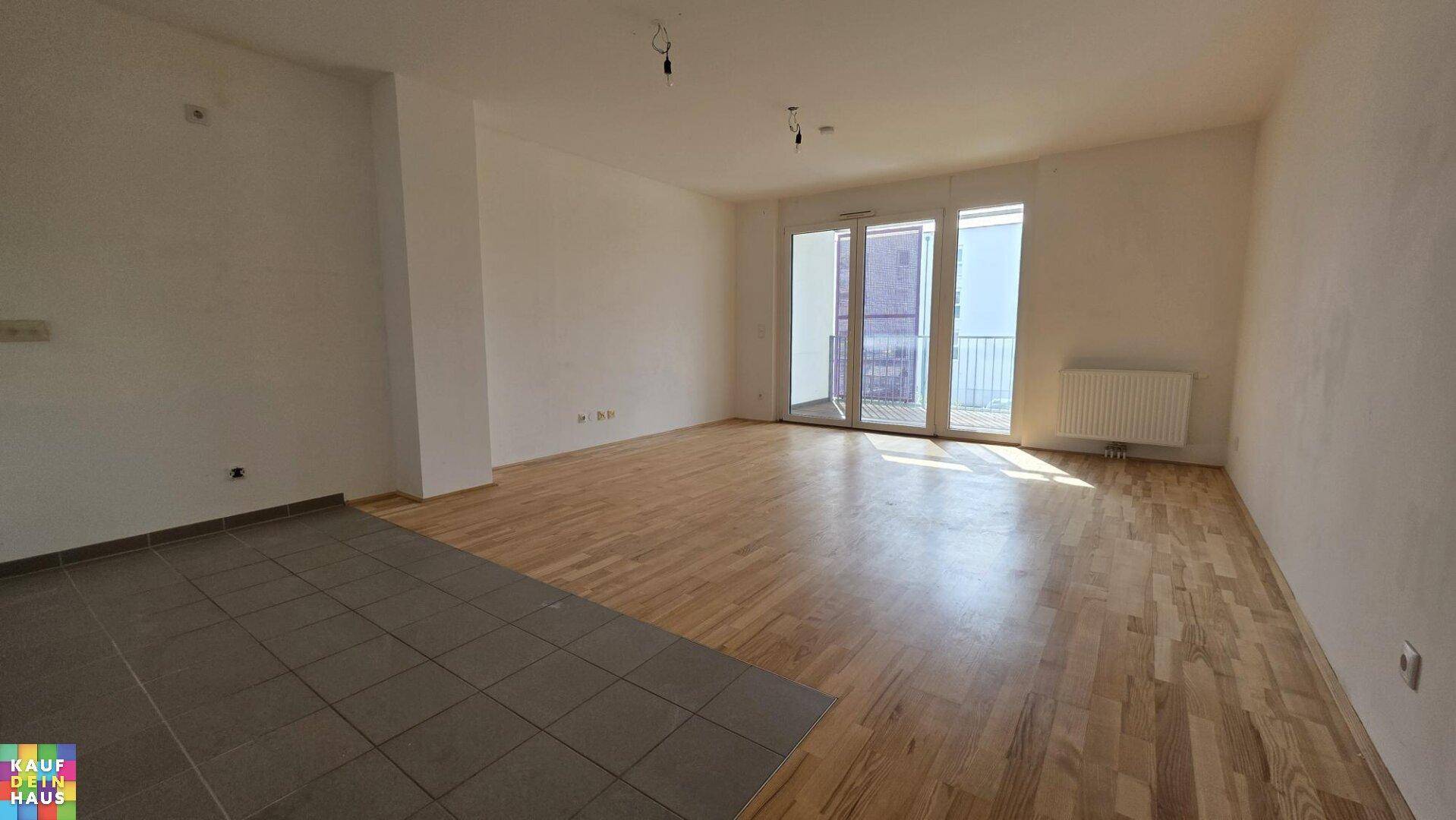Helles Wohnzimmer mit gemischtem Bodenbelag und großen Fenstern zum Balkon.