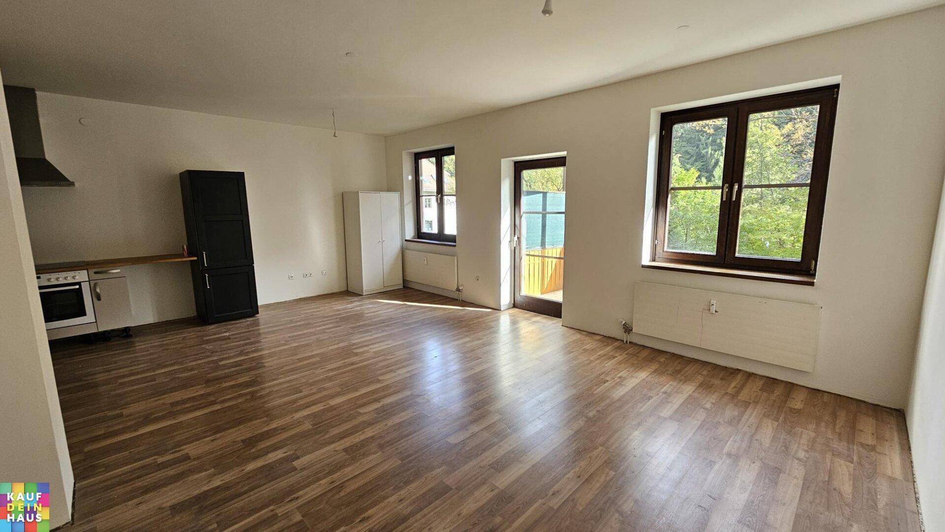 Geräumiger offener Wohnbereich mit Laminatboden, großen Fenstern und Zugang zu einem Außenbereich.