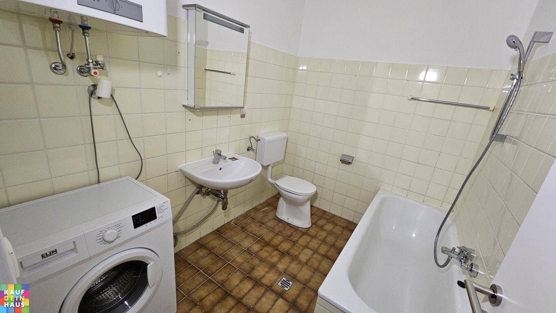 Badezimmer im 80er-Jahre-Stil mit Badewanne, Dusche, Waschbecken und Waschmaschine.