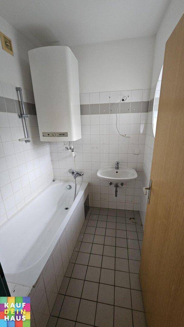 Badezimmer mit Badewanne, Waschbecken und Warmwasserbereiter, gefliest und funktional.
