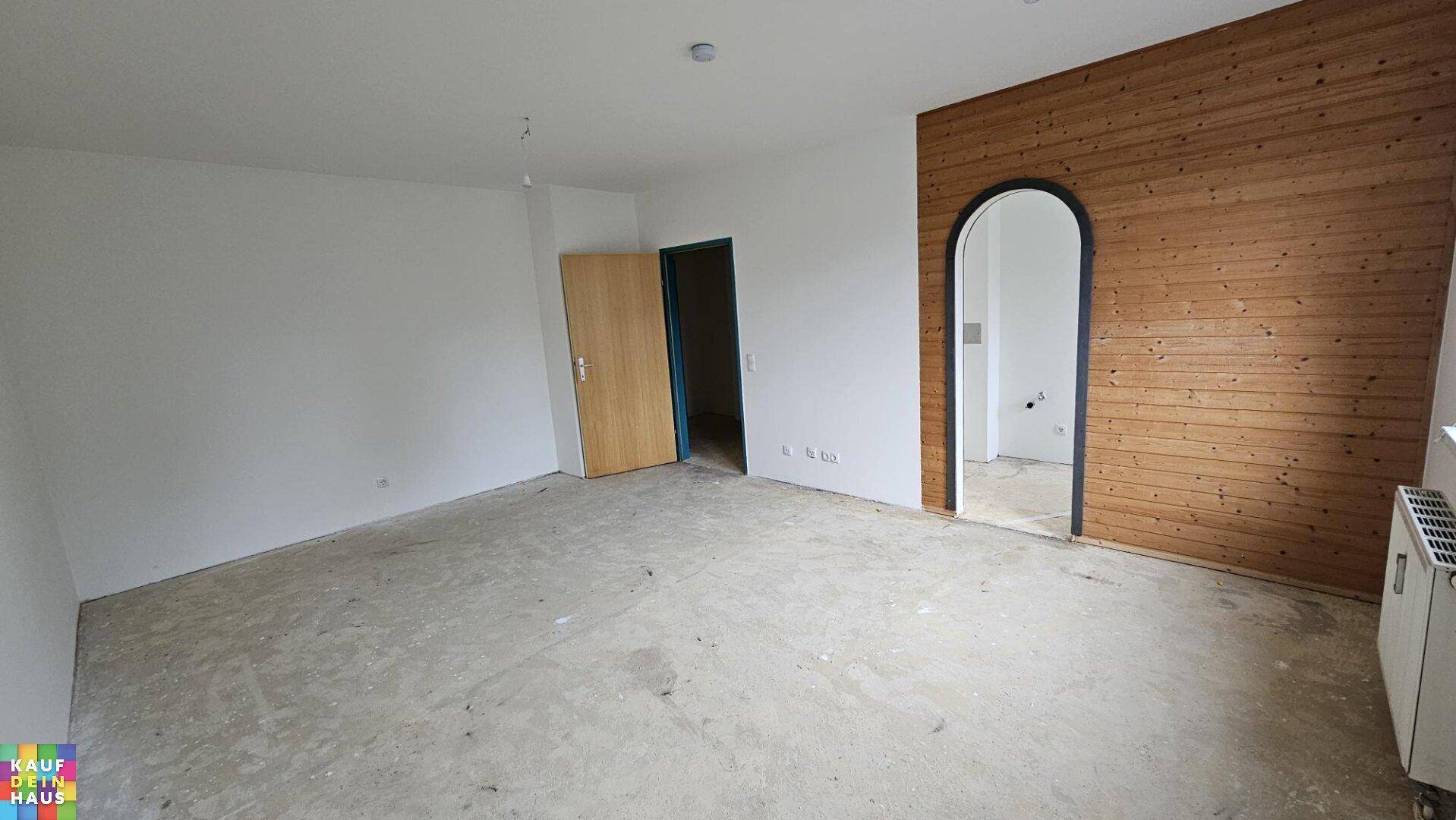 Geräumiger leerer Raum mit Holzwand, Rundbogen und unfertigem Boden, bietet viel Gestaltungspotenzial.