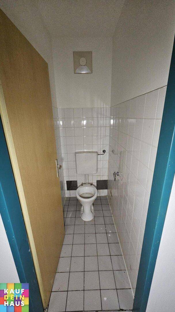 Kleines separates WC mit Toilette und weißen Fliesen an Wänden und Boden.