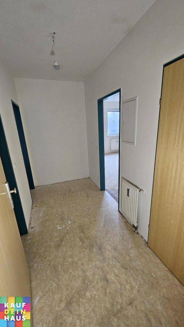Heller Flur mit mehreren Türen, Heizkörper und unfertigem Boden, verbindet verschiedene Räume.