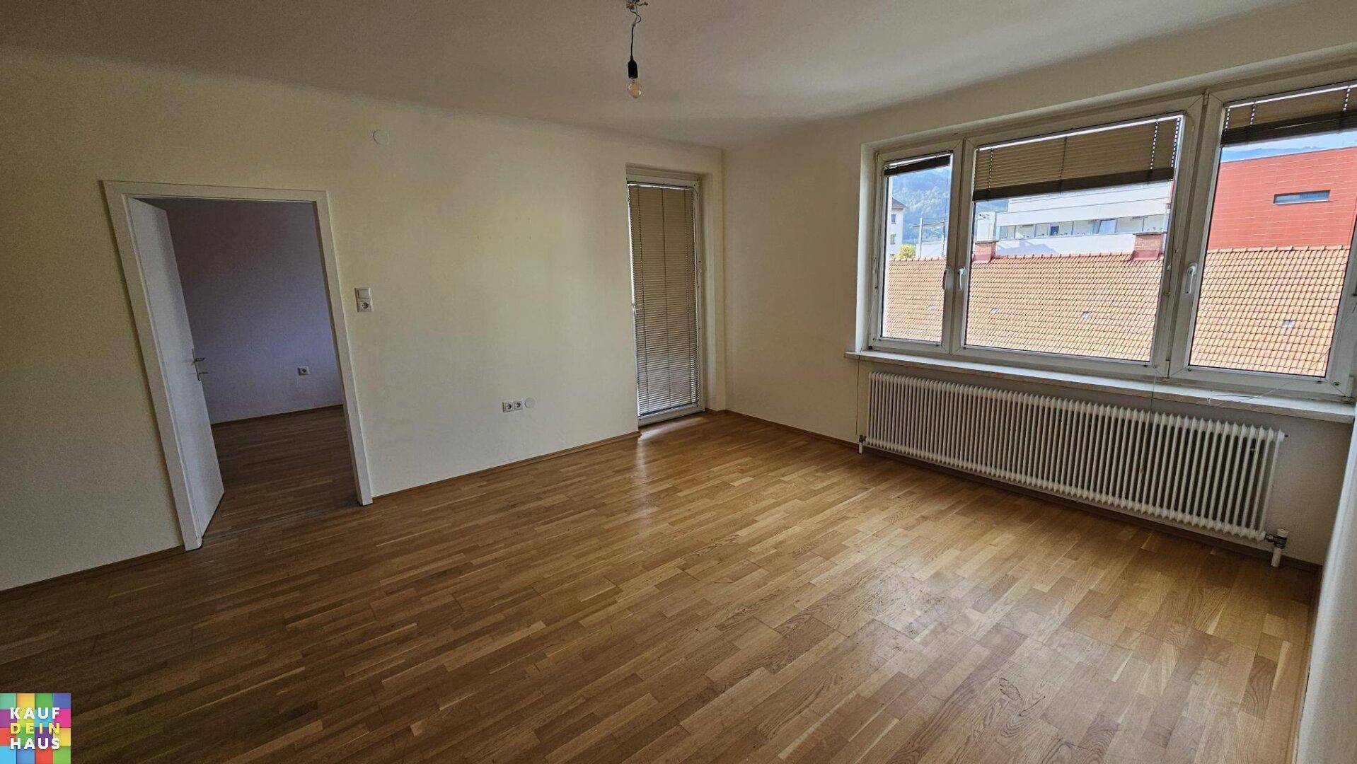 Geräumiges, leeres Zimmer mit hellem Parkettboden, großem Fenster und viel Tageslicht.
