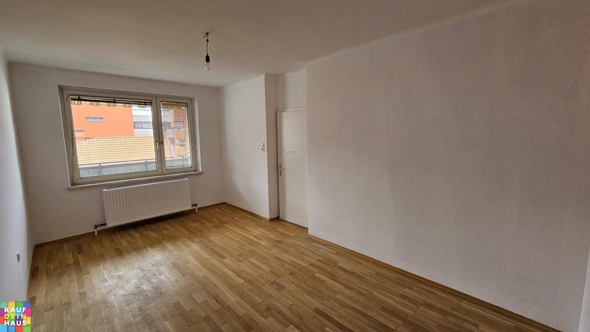 Freundliches Zimmer mit Holzfußboden, großem Fenster und Blick auf die Nachbarschaft.