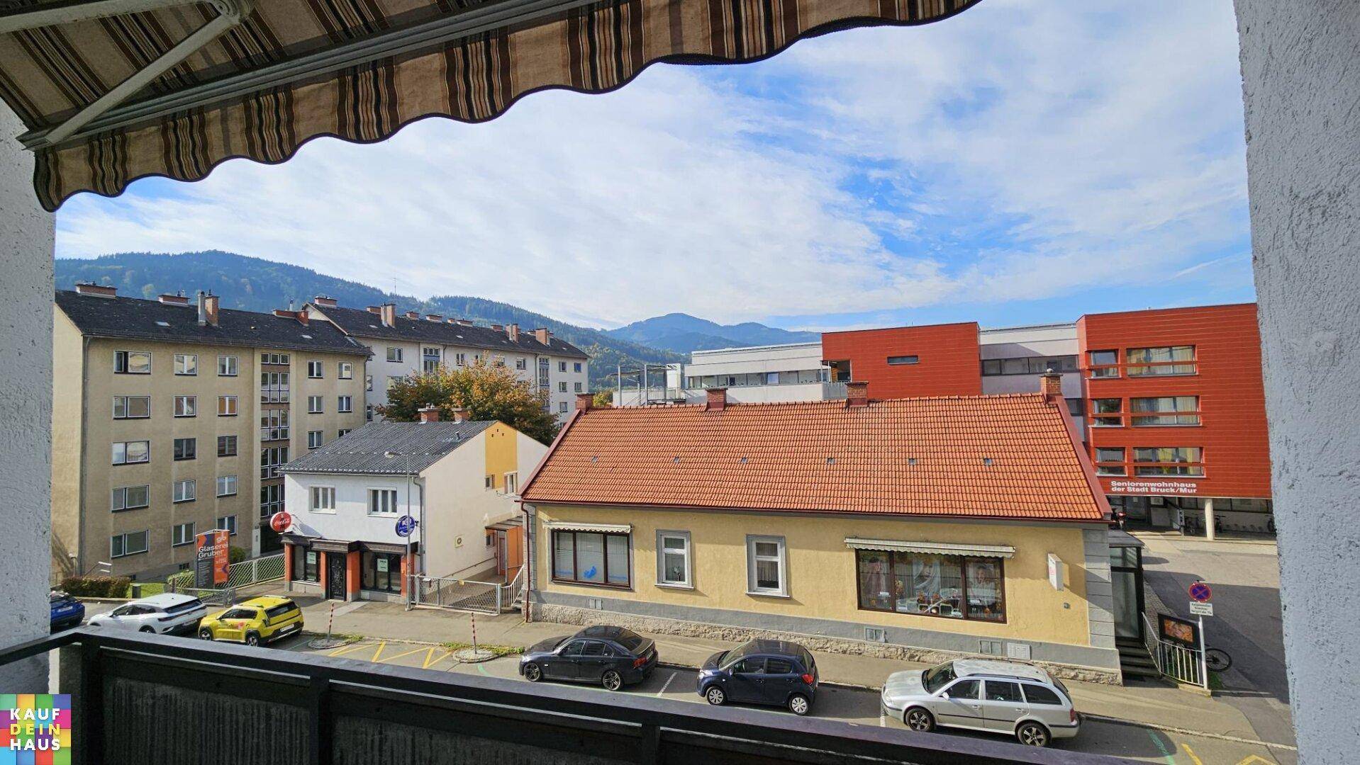 Weitblick über die Straße mit umliegenden Gebäuden und einer malerischen Bergkulisse im Hintergrund.