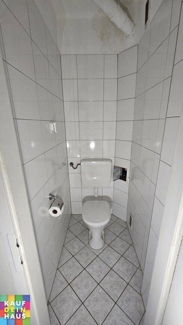 Separates WC mit weißen Wand- und Bodenfliesen und einer Standardtoilette.