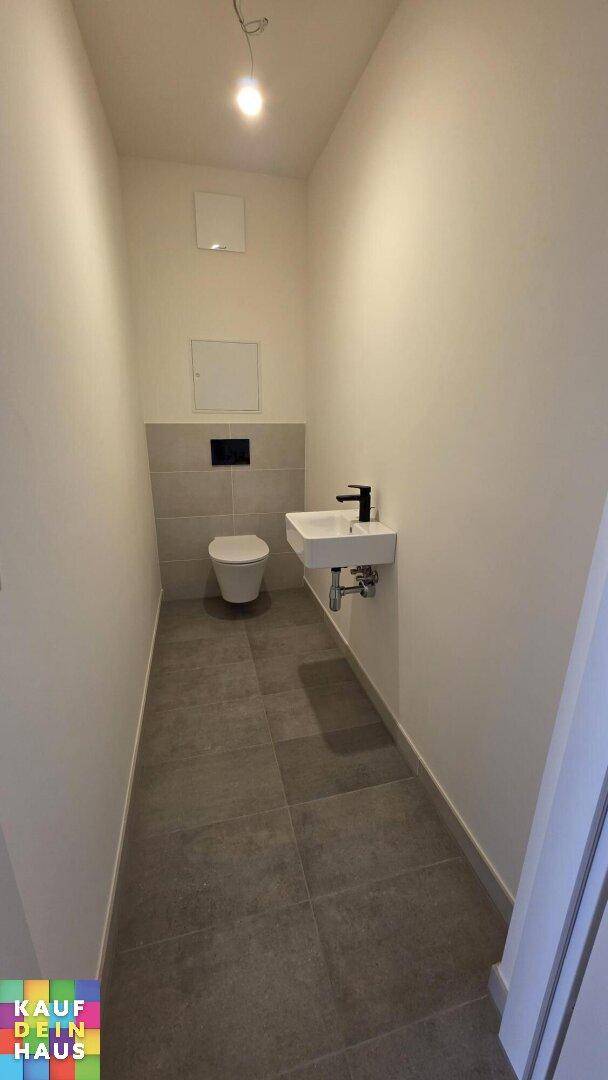Modernes Gäste-WC mit wandhängendem WC, kleinem Waschbecken und grauen Fliesen.