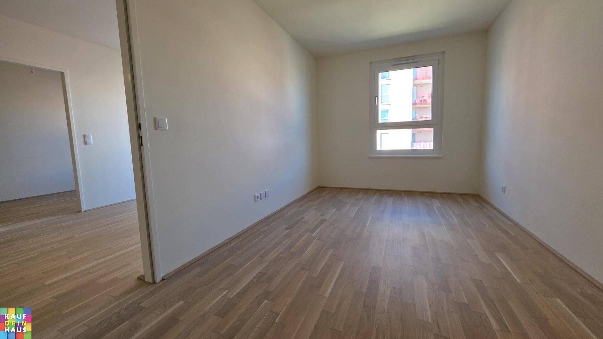 Geräumiges Schlafzimmer mit hellem Laminatboden, weißen Wänden und einem großen Fenster.