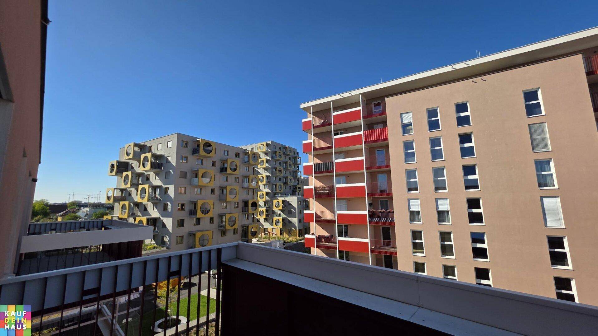 Blick vom Balkon auf moderne Wohngebäude, darunter eines mit auffälligen gelben Fassadenelementen.