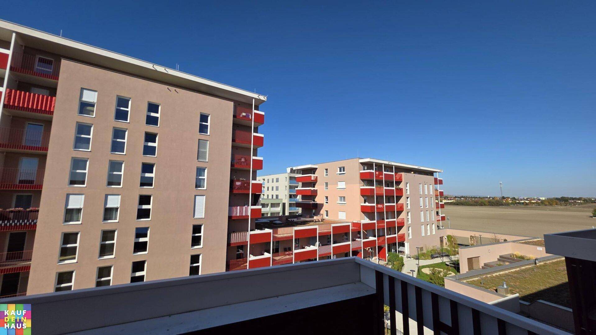 Weitblick vom Balkon über moderne Wohngebäude und grüne Felder am Horizont.