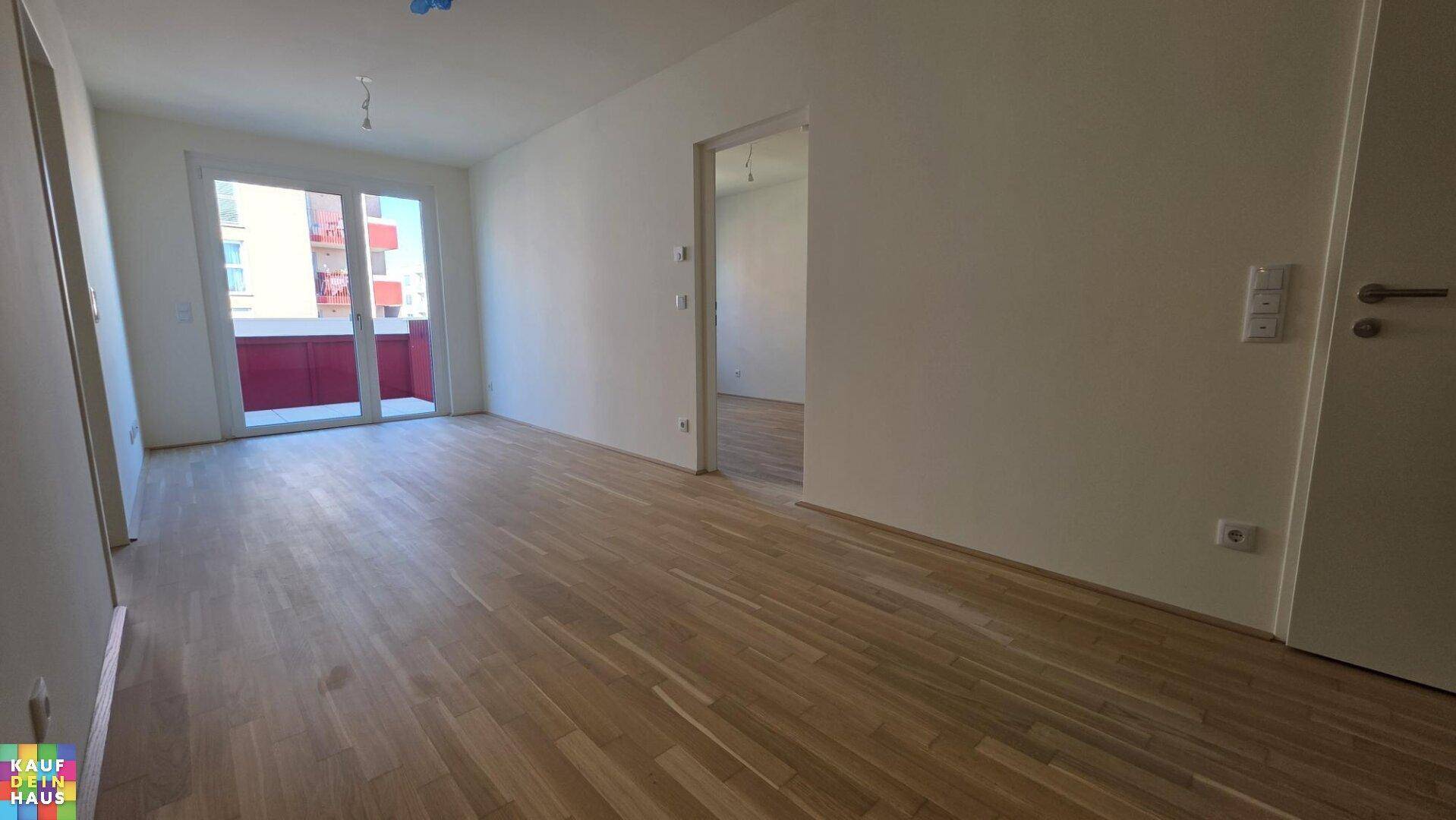 Heller Wohnraum mit Laminatboden, weißen Wänden und direktem Zugang zu einem Balkon.