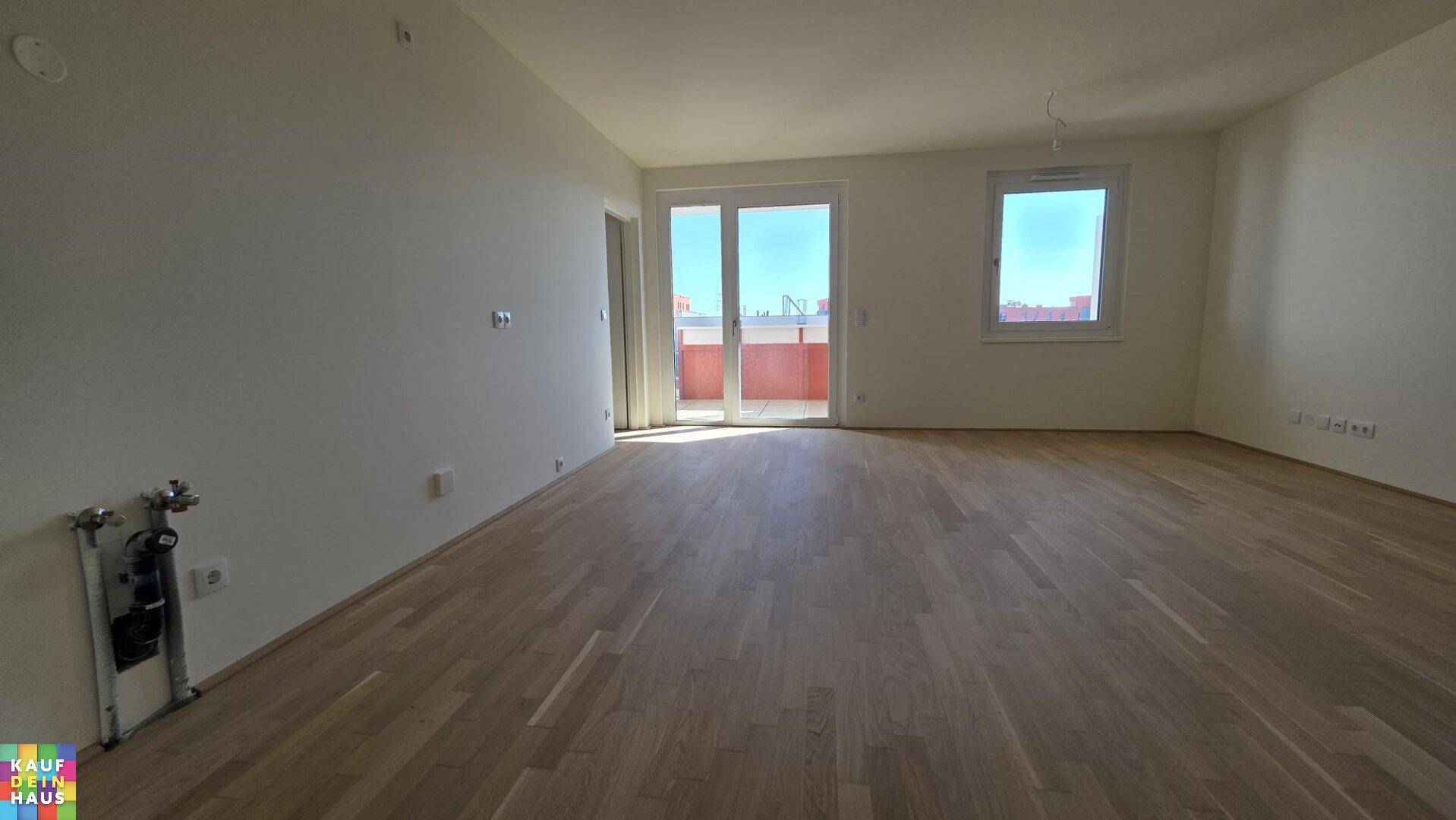 Geräumiges Wohnzimmer mit hellem Holzplankenboden und großen Fenstern für viel Tageslicht.