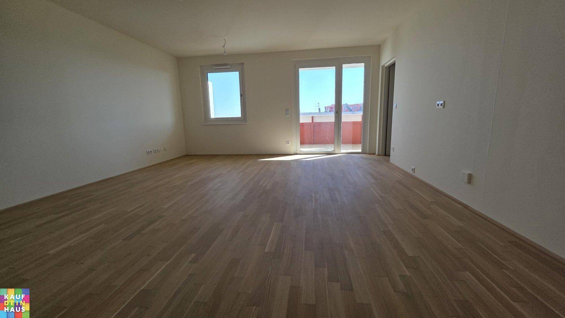 Großzügiger Wohnbereich mit Parkettboden und Zugang zu einem Balkon.