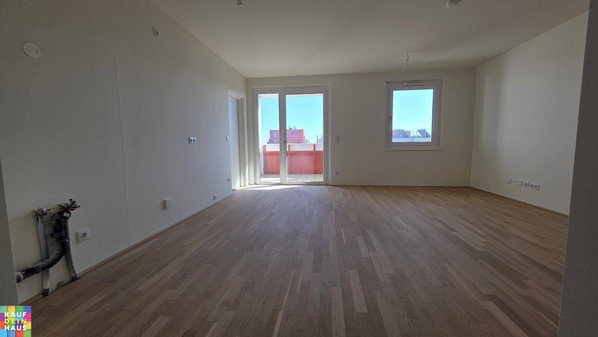 Großes, leeres Wohnzimmer mit hellem Holzparkett und direktem Zugang zum Balkon.