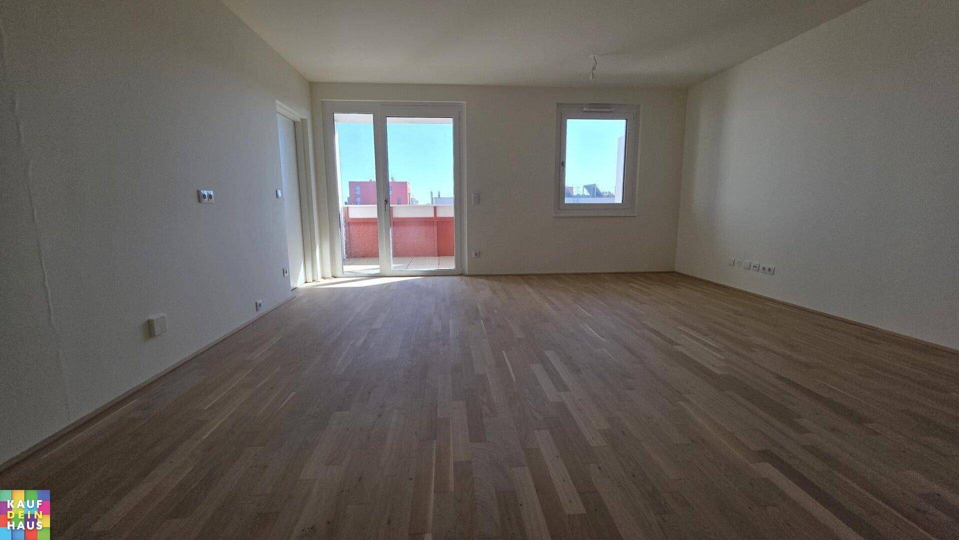 Geräumiges Wohnzimmer mit hellem Holzparkett und großen Fenstern, die viel Tageslicht hereinlassen.
