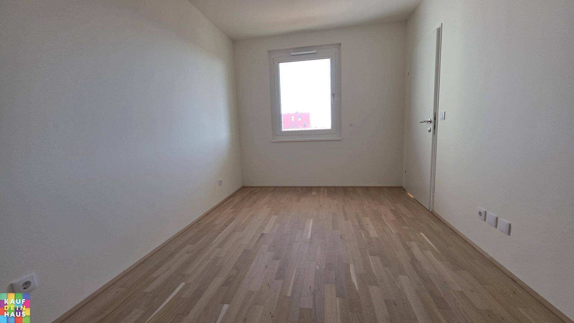 Helles Schlafzimmer mit Holzparkett und einem Fenster, das viel Tageslicht bietet.