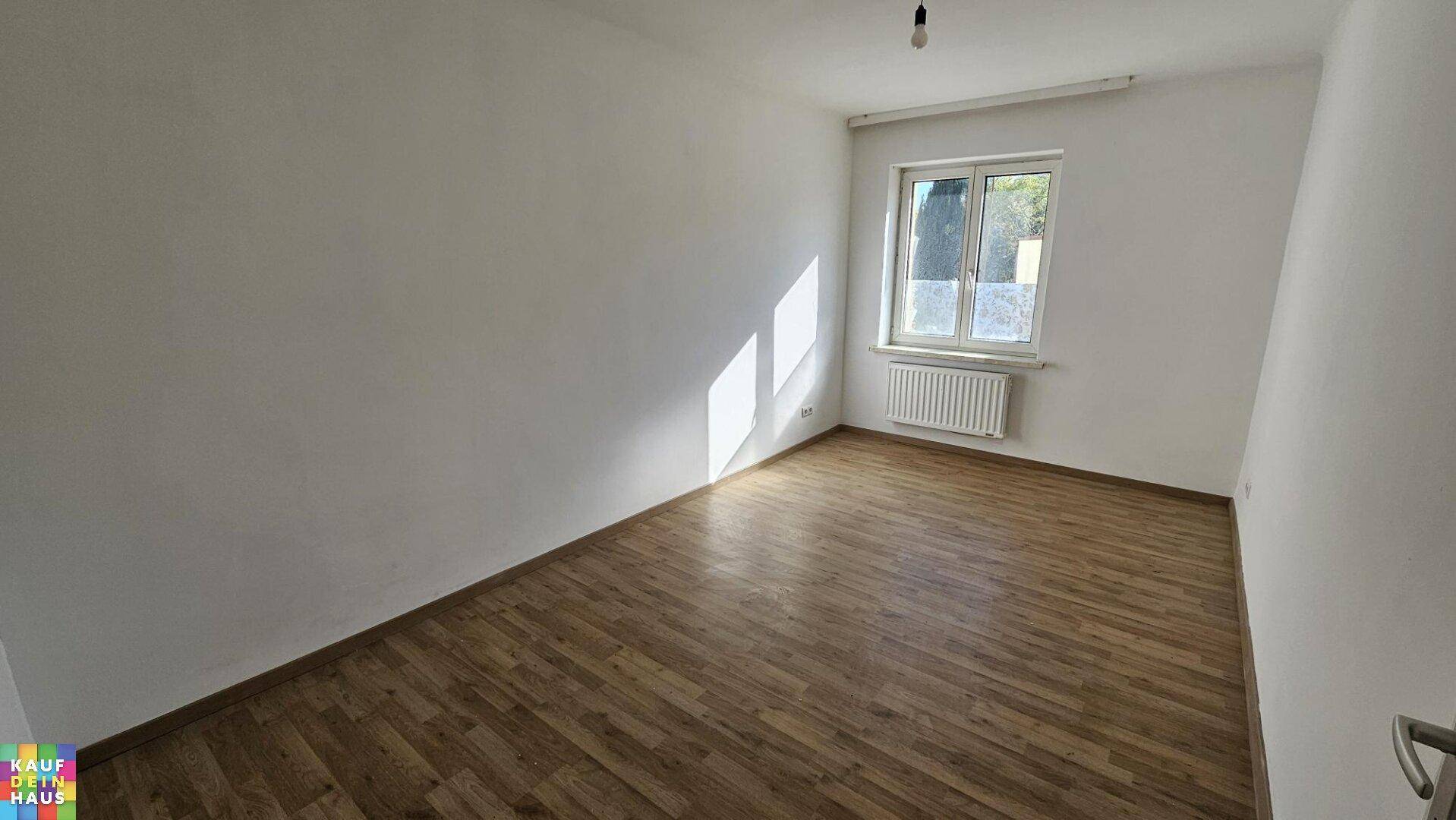 Geräumiges Zimmer mit Laminatboden und großem Fenster, das viel Tageslicht hereinlässt.