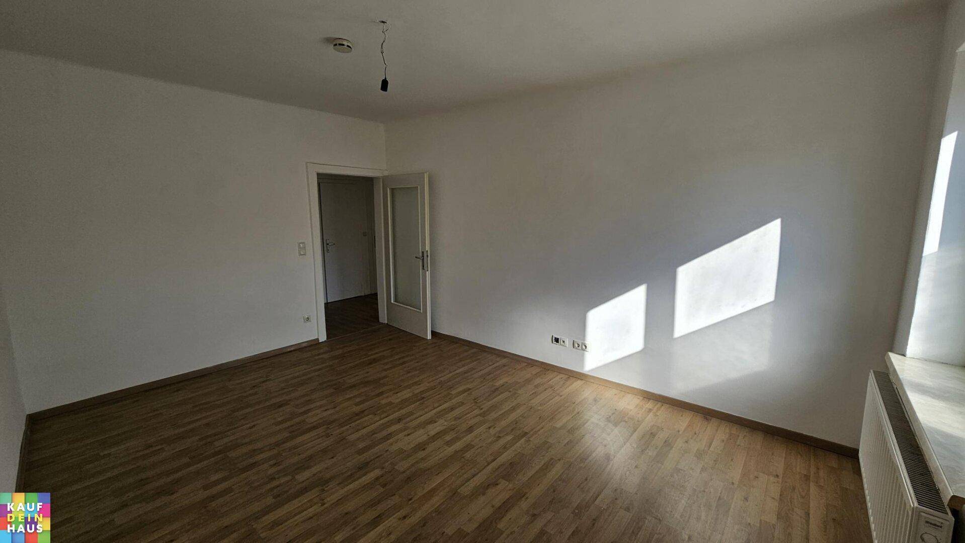 Lichtdurchflutetes Zimmer mit Laminatboden und Zugang zu weiteren Räumen, ideal für Wohnzwecke.
