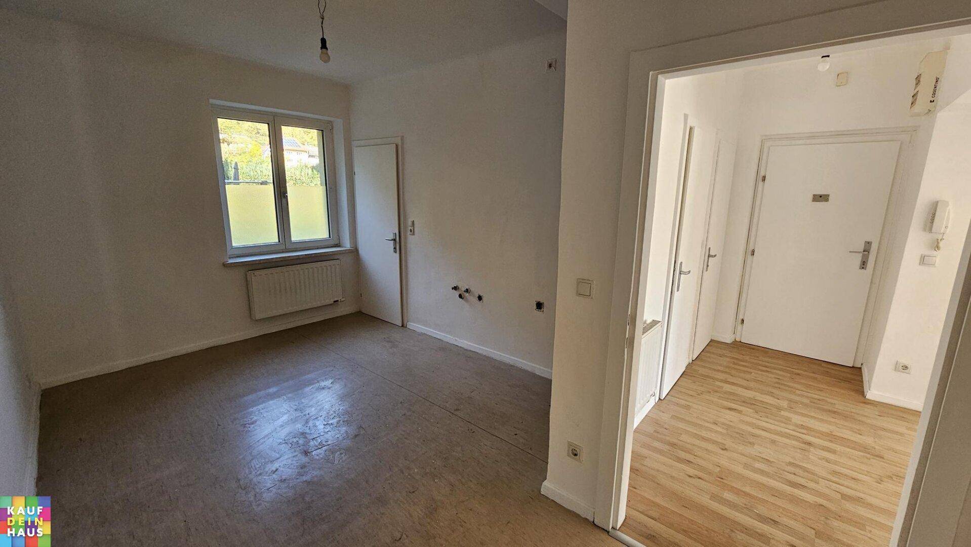 Leeres Zimmer mit hellem Bodenbelag und Fenster, bietet Zugang zu einem Flur mit Laminat.