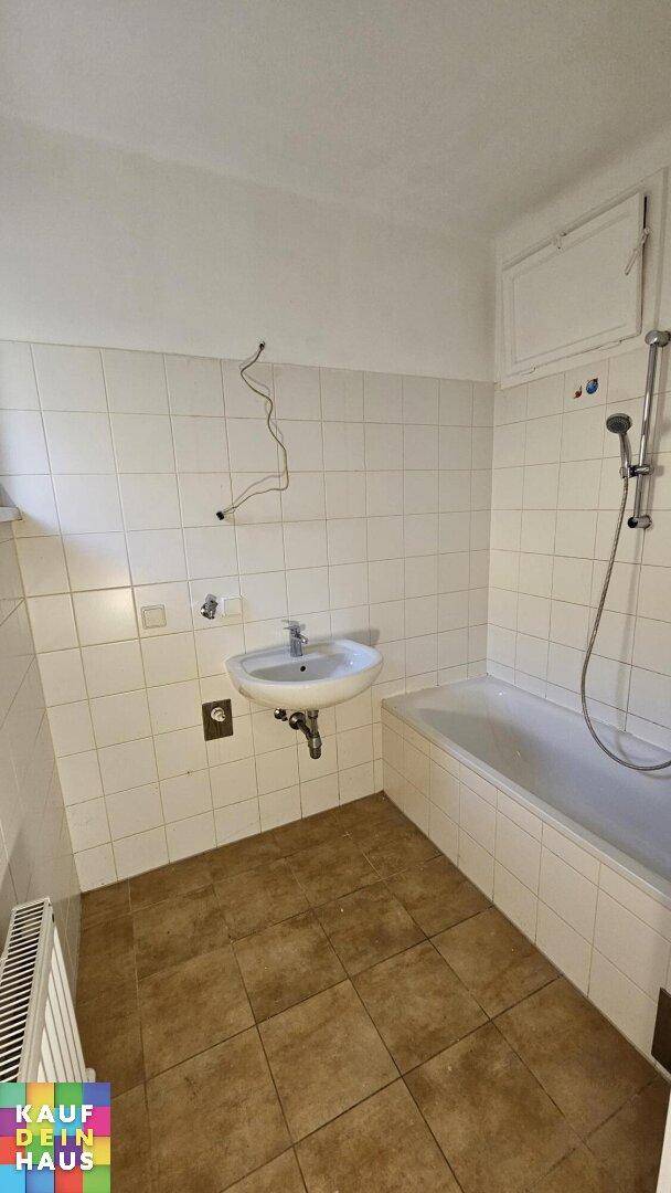Gefliestes Badezimmer mit Badewanne, Duschvorrichtung und Waschbecken, in gutem Zustand.
