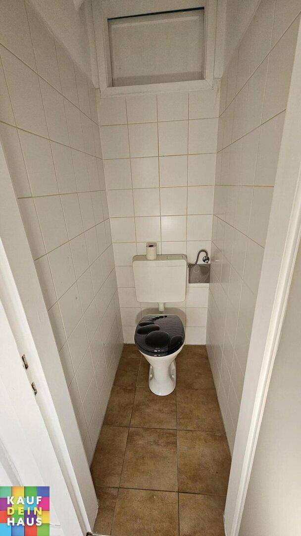 Kleines, gefliestes WC mit Toilette und Oberlichtfenster, funktional und sauber.