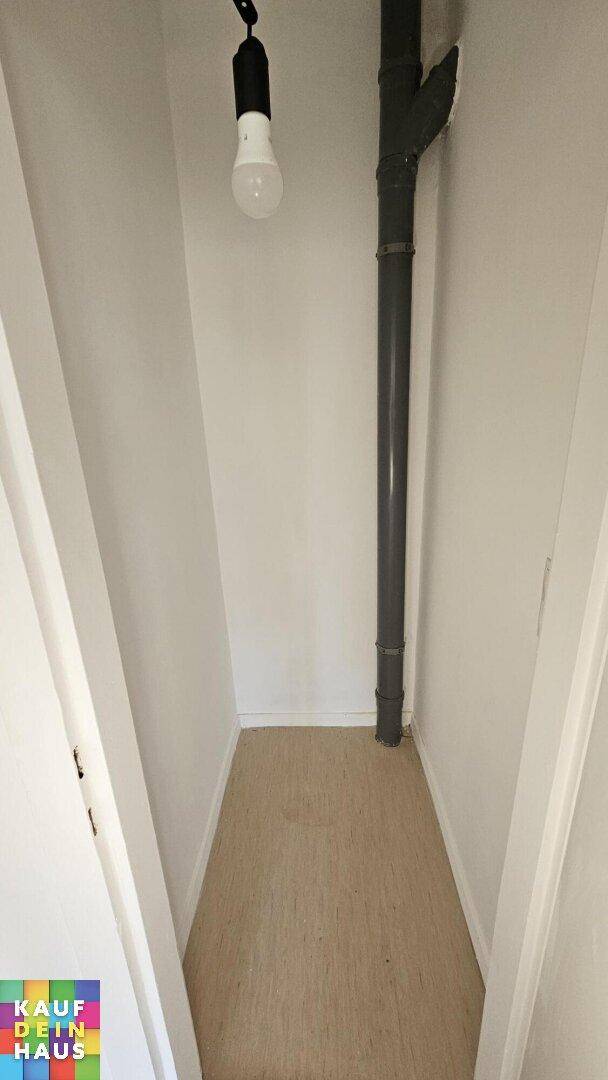 Schmaler Abstellraum mit freiliegendem Rohr und einfacher Beleuchtung, praktisch für Lagerzwecke.